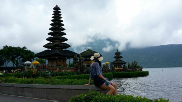 a girl with a hat looking at the Bratan temple and the foggy sky above the lake, centrla Bali 