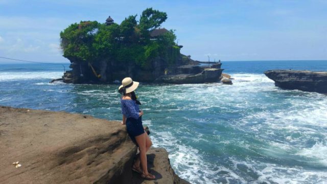 a girl with a hat looking at the Tanah Lot temple island