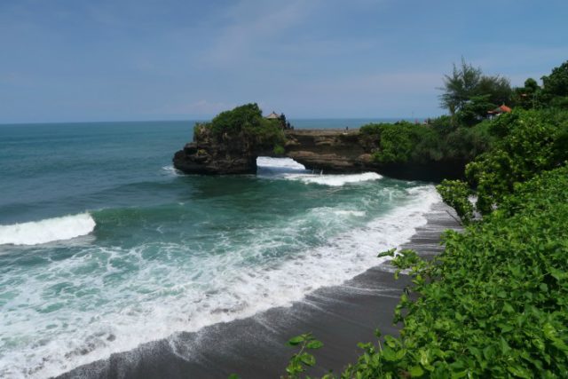 Tanah Lot temple on a cliff and big waves crushing the black sand volcanic beach below 