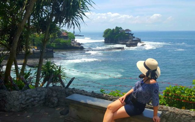A girl with a hat looking at the Tanah Lot temple in central Bali 
