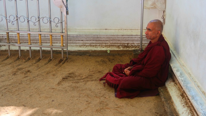 A Buddhist monk in the red gown meditating in the Bodhi Tree Temple in Sri Lanka 