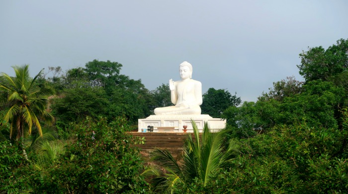 a huge white Buddha statue surrounded by green jungle and palm trees in Mihintale in Sri Lanka 