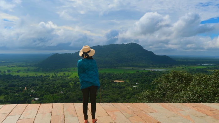 a girl with a hat staring at the lush and green jungle landsacape in Mihintale in Sri Lanka - the view from Maha stupa 
