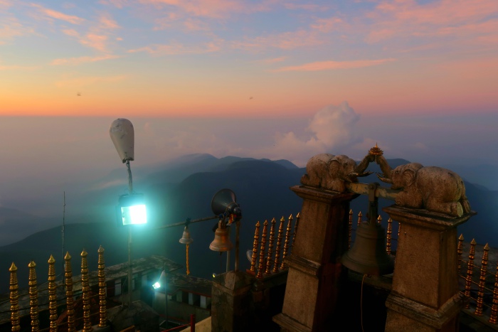 the wish bell and two stone elephants above it surrounded by pastel sunset sky at the top of sri pada adams peak in sri lanka