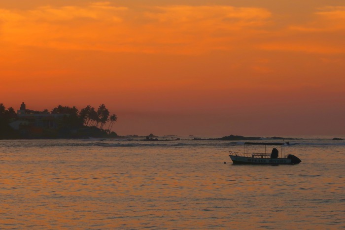 orange sky and a boat floating on the sea before the sunrise in unawatuna sri lanka 