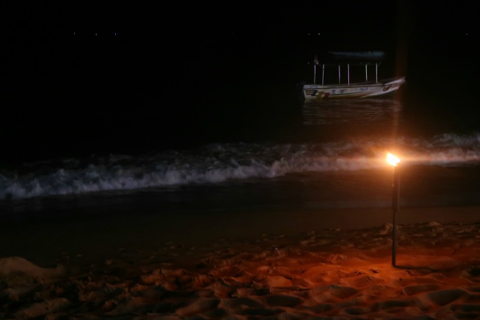 a fire torch on the beach at night and a small boat floating in the sea in unawatuna sri lanka 