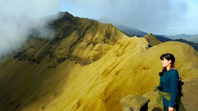 a girl standing on the edge of an active volcano crater - bromo volcano in java indonesia 