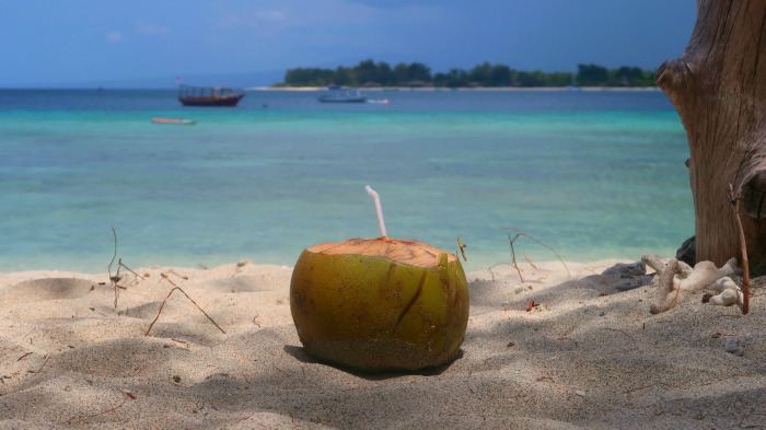 a green coconut with a straw on a sandy beach and turquoise blue sea in gili trawangan indonesia
