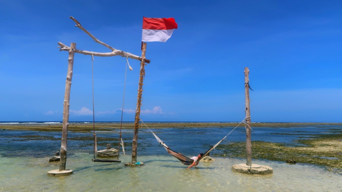 a girl enjoying on a hammock in the middle of the sea and an indonesian flag in gili trawangan indonesia