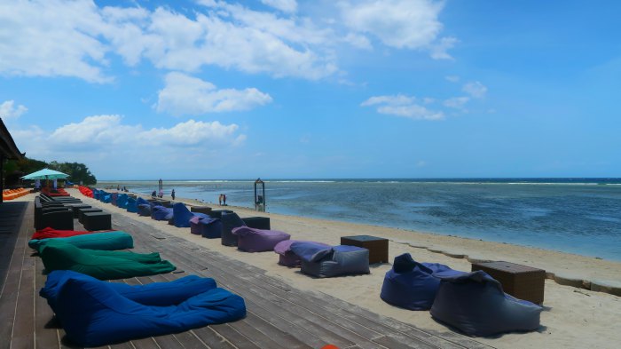 a lounge area with colourful laying sofas on a sandy beach in gili trawangan indonesia
