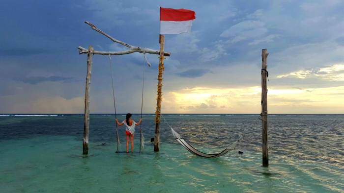 a girl watching the sunset on a swing in the middle of the sea and the indonesian flag in gili trawangan indonesia