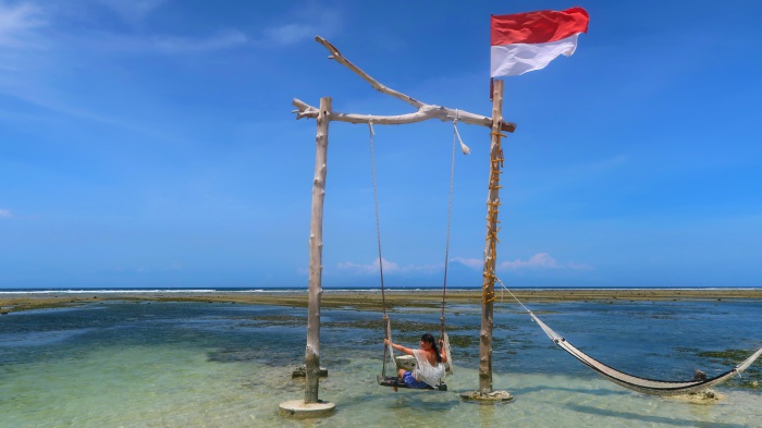 a girl on a huge swing and an indonesian flag in the middle of the sea in gili trawangan indonesia