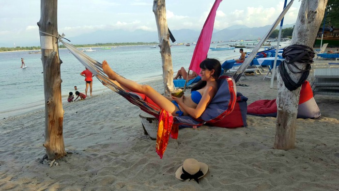 a girl enjoying on a hammock with coconut in her hands on a sandy beach in gili trawangan indonesia