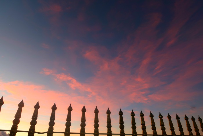 the golden fence around the temple at the top of sri pada adams peak in sri lanka and the pastel pink sunset sky 